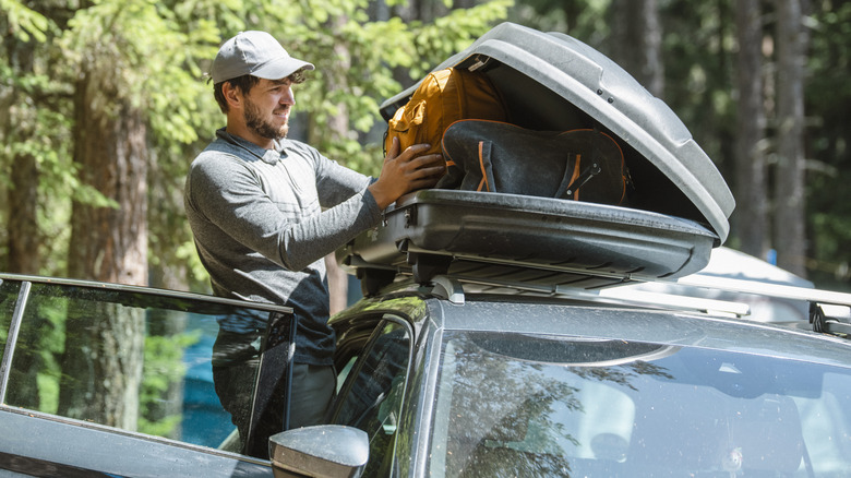 A man adding luggage on a roof carrier.