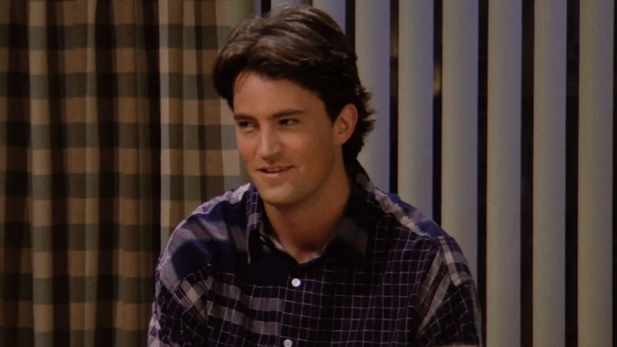 Chandler Bing smiling with a center part and a flannel shirt in Friends.