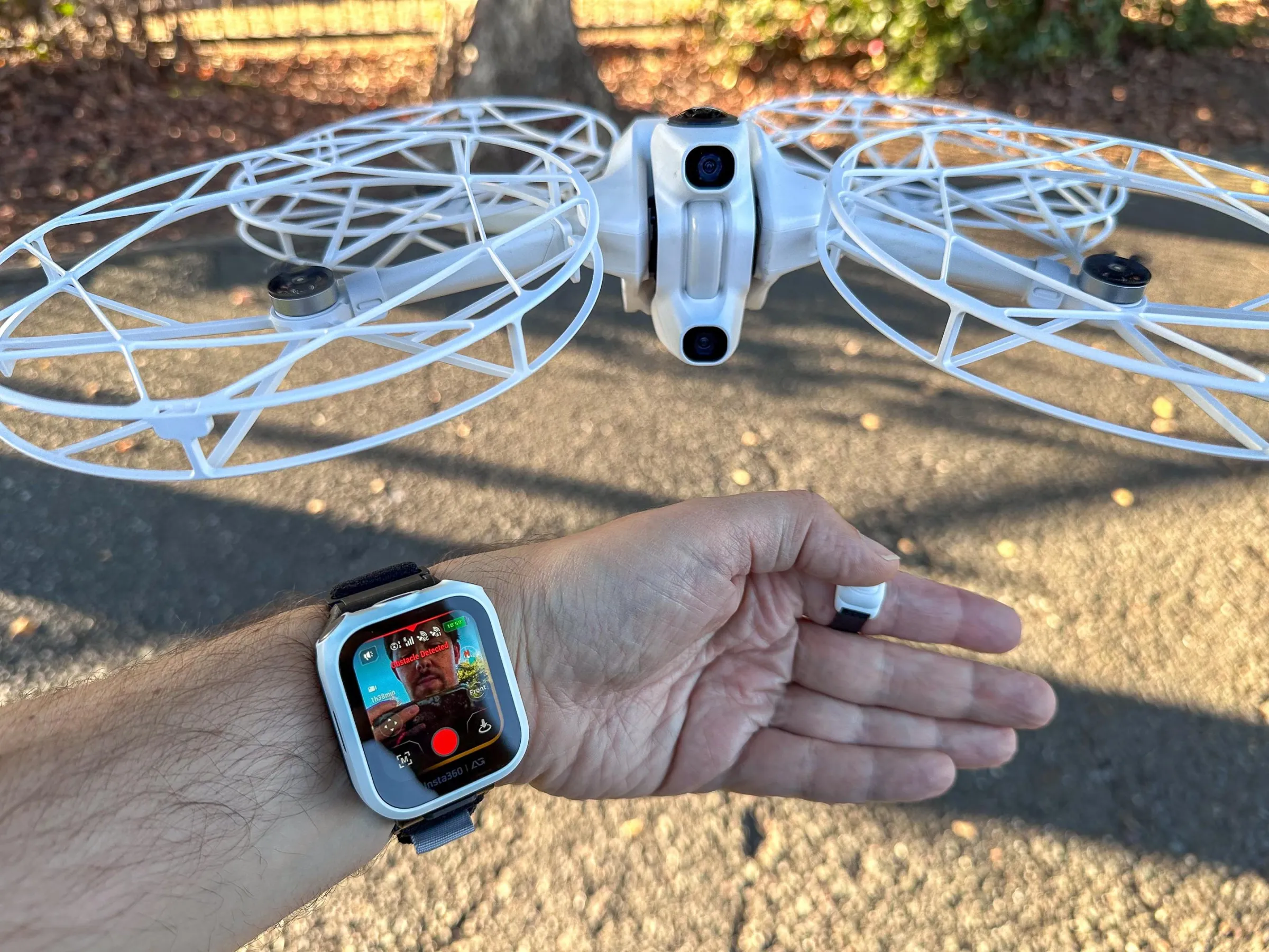 A wristwatch screen controls a drone flying right above the person’s hand. A ring controller is also visible.