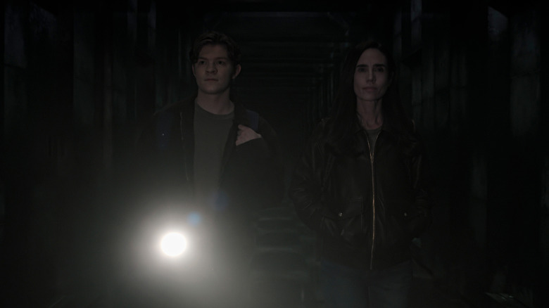 Oakes Fegley as Charlie Dessen standing in a dark hallway and holding a flashlight next to Jennifer Connelly as Daniela Dessen in Dark Matter