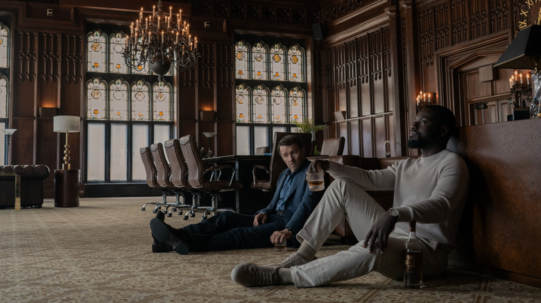 Dayo Okeniyi as Leighton Vance holding a drink and sitting against a counter next to Joel Edgerton as Jason Dessen in a conference room in Dark Matter