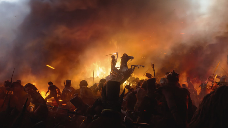 Someone wields a sword on horseback on a fiery battlefield in Wildwood